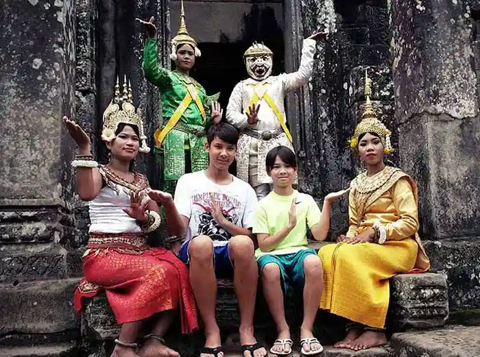 Family posing with traditional dancers in costume at Angkor temple in Cambodia.